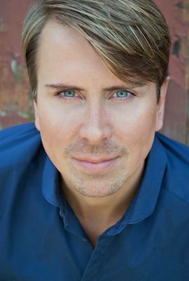 Das Portrait zeigt Nadine Werner mit langen, blonden Haaren. Sie lehnt mit dem Rücken an einer grauen Wand und sieht lächelnd in die Kamera.