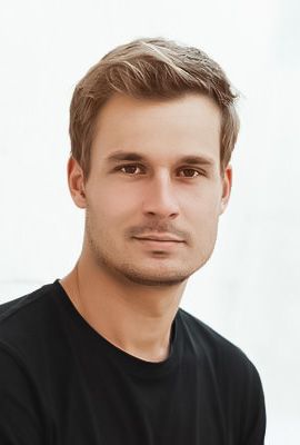 Das Bild zeigt Robert Schmelcher, Darsteller bei Best of Musicals, mit lockigen hellbraunen Haaren und ernsthaftem Blick. Er trägt ein weißes T-Shirt.