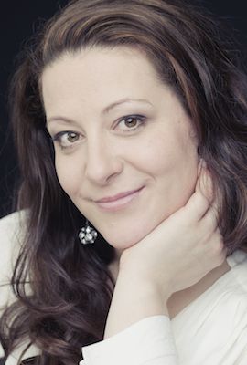 Das Bild zeigt Nadine Hammer, Darstellerin bei Best of Musicals, mit langen, gewellten braunen Haaren und einem freundlichen Lächeln. Sie trägt ein rotes Oberteil, einen schwarzen Blazer und große Ohrringe.